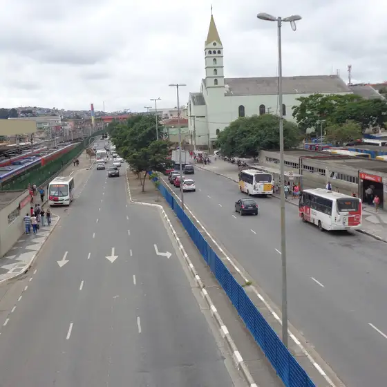 Rua Salvador Gianetti, em Guaianases, com ônibus e a igreja ao fundo